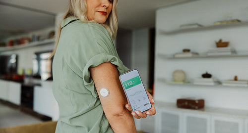 Senior woman checks glucose monitor with smartphone at home