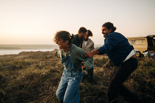 Playful friends chase each other on a windy beach at sunset