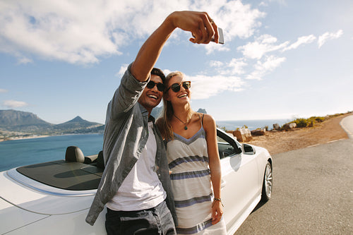 Couple standing by their car taking selfies