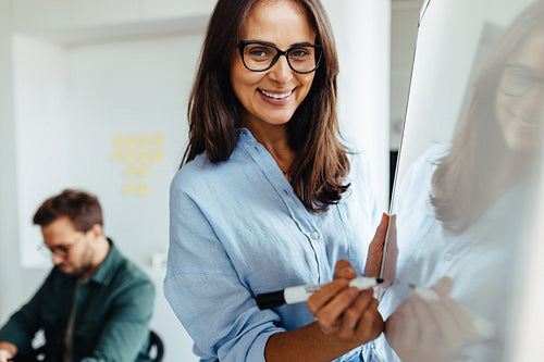 Happy business woman writing her ideas on a board during a meeting