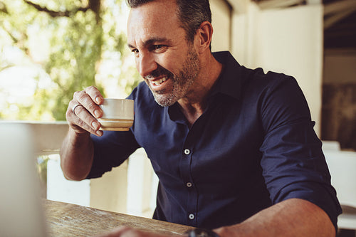 Man having coffee at cafe and looking at laptop