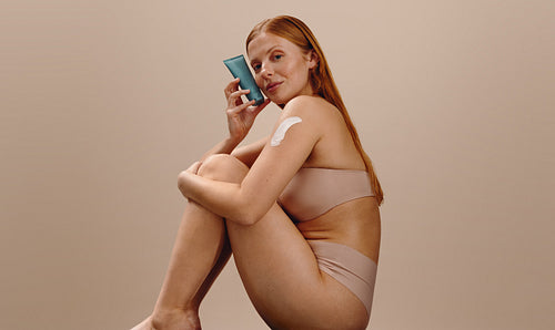 Woman applying body lotion while holding product tube