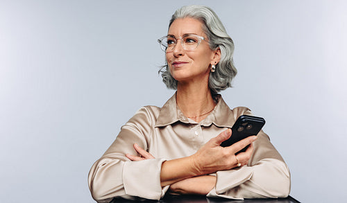 Mature professional woman smiles holding phone with arms crossed