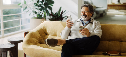 Senior drinks coffee while using a smartphone at home