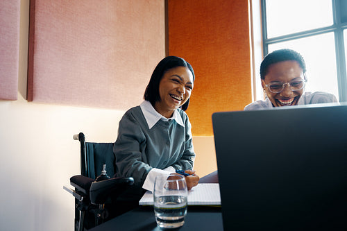 Two young women laughing together while working on a laptop