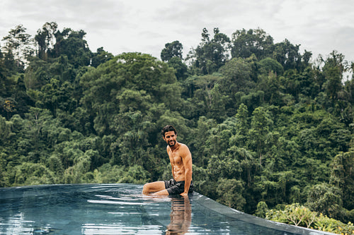 Happy young man sitting in swimming pool