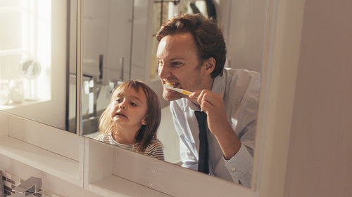 Father teaching daughter how to brush teeth
