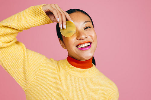 Woman with a two tone lipstick looking at the camera and holding a yellow cap from a beauty product