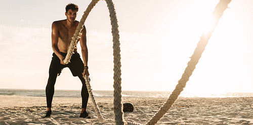 Man doing workout using battling ropes at the beach