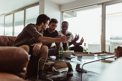Three friends sitting on a sofa showing a game on the phone
