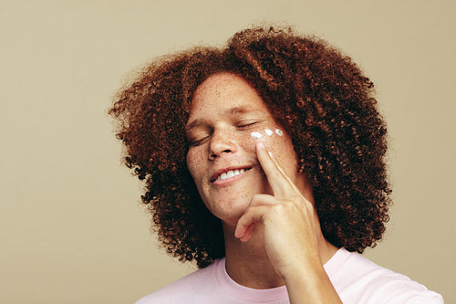 Man with curly ginger hair applies beauty cream to his face