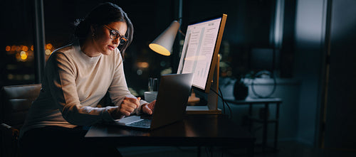 Nighttime productivity: Young businesswoman typing on laptop in home office