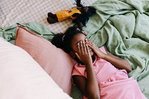 Playful black girl relaxing on bed with her doll
