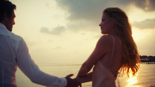 Romantic couple walking hand in hand on a beautiful tropical beach at sunset