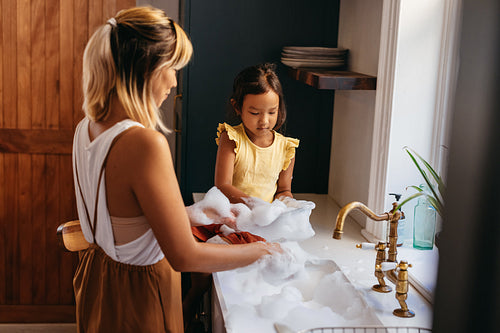 Little girl learning how to wash dishes at home