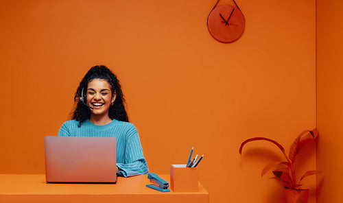 Smiling woman working on laptop in monochromatic orange office, engaging in digital marketing and online shopping