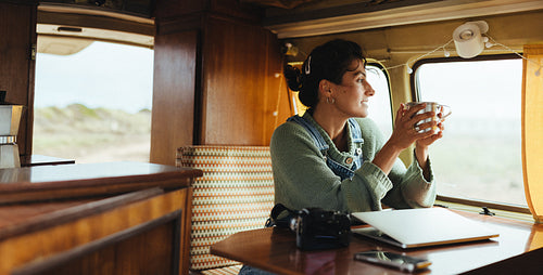 Traveler woman in a cozy camper van enjoying morning coffee with laptop and camera