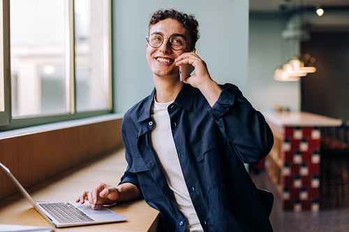 Smiling young professional man on a phone call while using a laptop