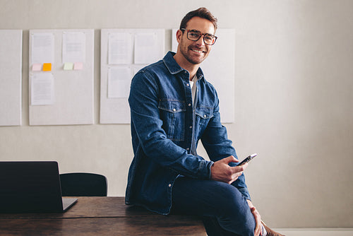 Happy businessman smiling at the camera while sitting on his desk