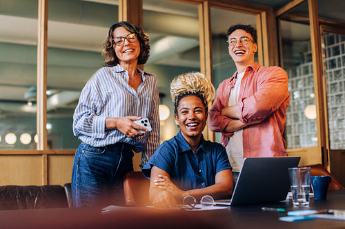 Smiling coworkers gathered around a laptop in a casual office setting