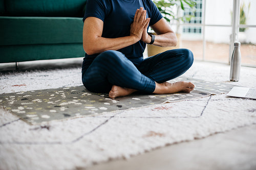 Woman meditating in prayer pose, sitting on the floor at home