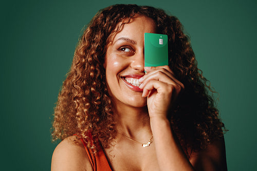 Playful woman brings a banking card close to her face in a green portrait