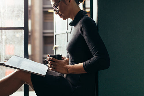 Relaxed woman on window sill reading a book