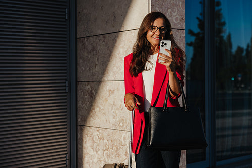 Businesswoman smiling while checking her phone outdoors near a building