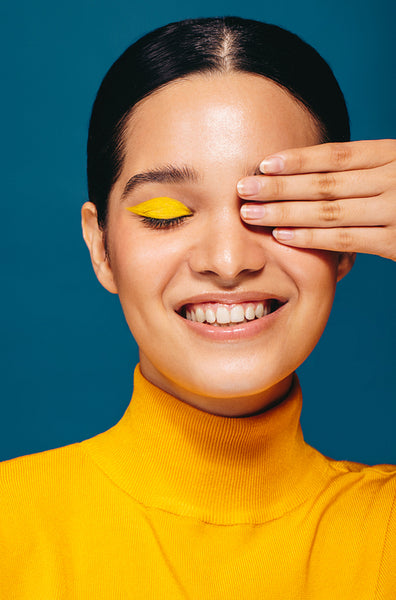 Wearing vibrant eye shadow, woman covers her eye in a studio