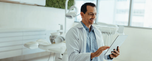 Male dentist using a tablet in clinic beside dental equipment