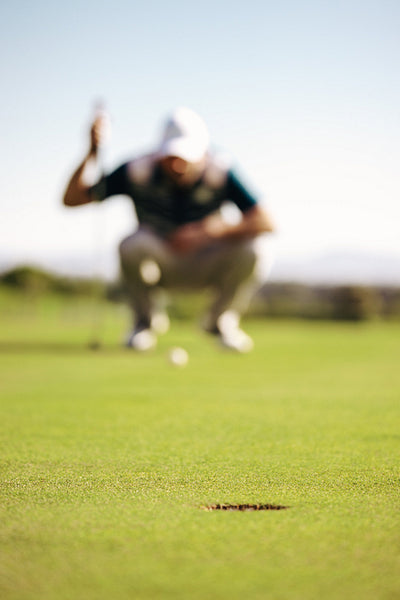 Close-up of golf hole with player blurred in the background on the putting green
