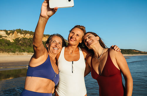 Three cheerful women enjoying a seaside selfie on a sunny day