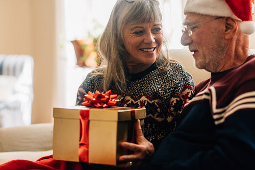Senior couple sitting at home celebrating christmas holding a gift box