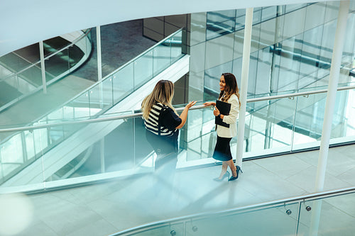 Female colleagues discussing business in a modern corporate office walkway
