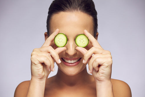 Woman holding slices of cucumber over eyes