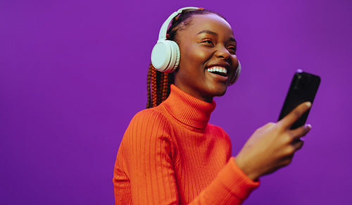 Young woman listening to music on purple background