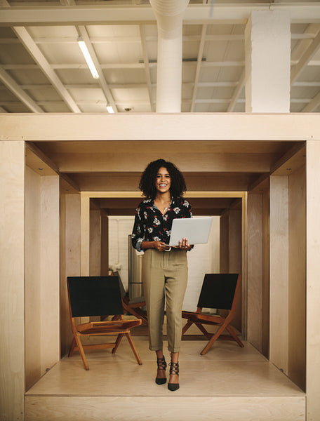 Smiling woman entrepreneur standing in office holding laptop