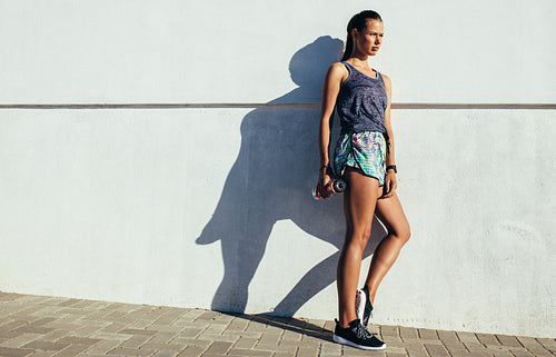 Fitness woman leaning to a wall and looking away