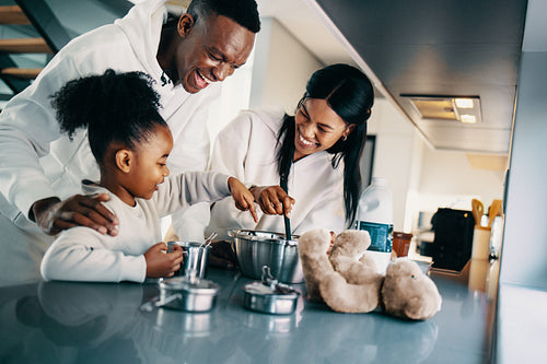 Parents making food with their little daughter in the kitchen; black family preparing breakfast together on the weekend