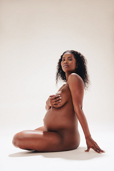 Black woman sitting naked in a studio, feeling comfortable in her pregnancy body
