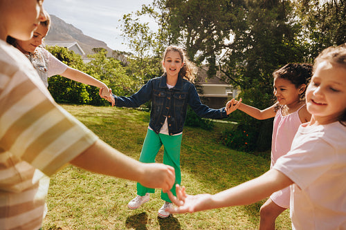 Children playing together in a sunny garden holding hands and smiling