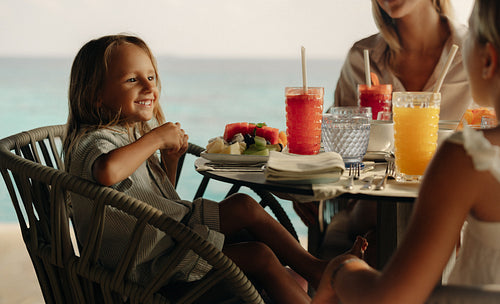 Children enjoying breakfast with mother by the seaside, smiling and happy