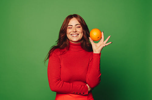 Cheerful woman holding fresh citrus fruit on green background