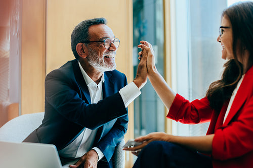 Senior executives high-fiving during a professional meeting in a bright office
