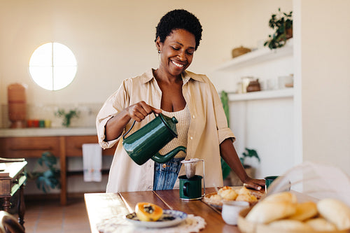 Brazilian woman smiling while pouring herself drip coffee at the breakfast table
