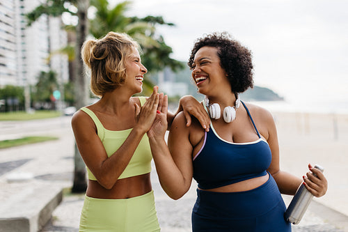 Happy fitness buddies high fiving each other on a beach promenade