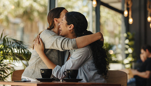 Best friends meeting in cafe giving each other a hug