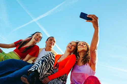 Friends share a selfie with a smartphone outdoors under clear sky
