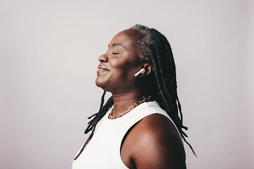 Cheerful mature woman listening to some music on bluetooth earbuds