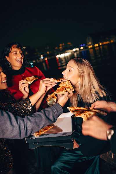 Group of friends sharing pizza by the water during a city night out
